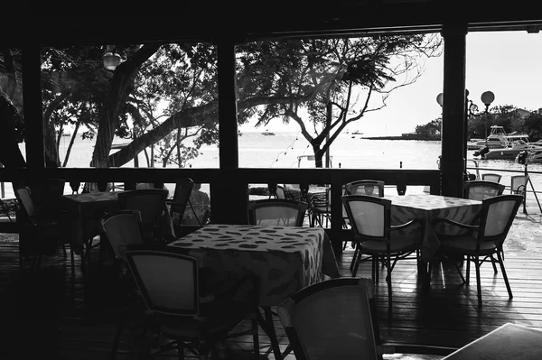 Black and white photo of empty open air restaraunt near sea at sunset