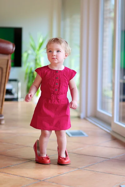 Lovely toddler girl walking indoors in mom\'s red shoes