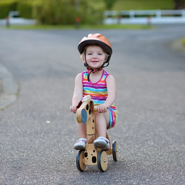 Happy little child in safety helmet riding wooden tricycle