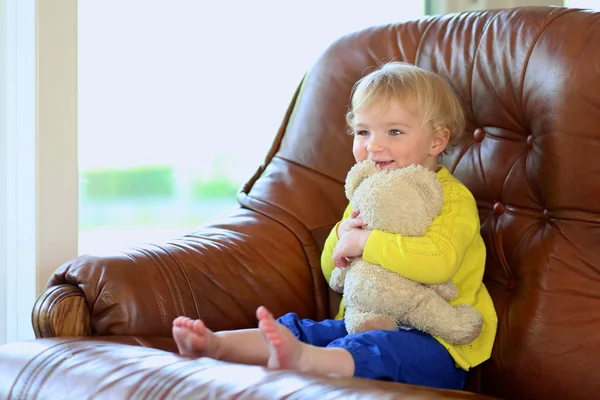 Little girl sitting on sofa holding teddy bear