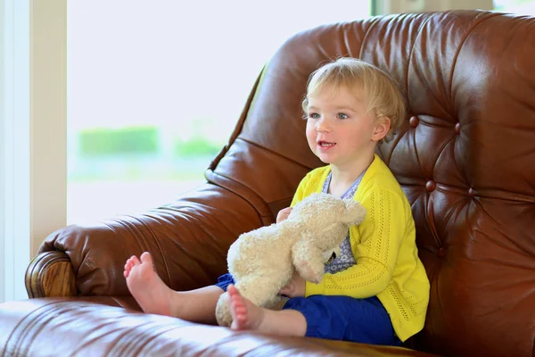 Little girl sitting on sofa holding teddy bear