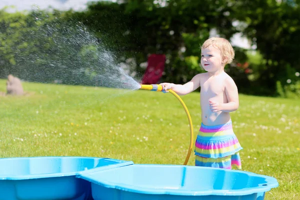 Happy little girl playing with water hose in the garden