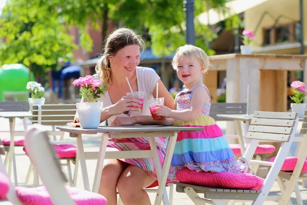Young mother and little daughter enjoying summer drinks in outdoors cafe