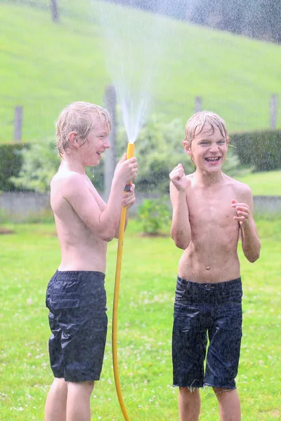 Two happy boys playing in the garden with watering hose