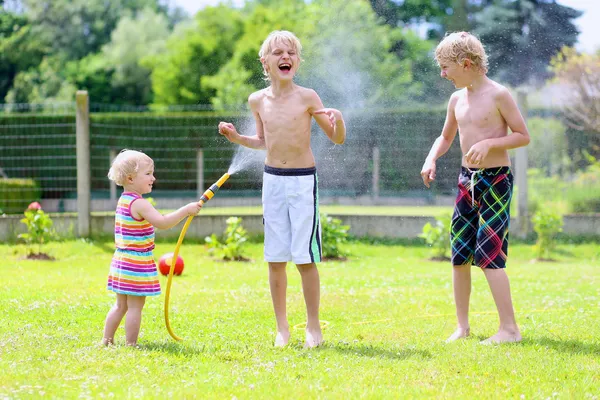 Group of happy children playing in the garden with watering hose
