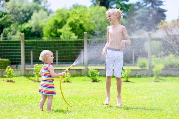 Brother and sister playing in the garden with watering hose