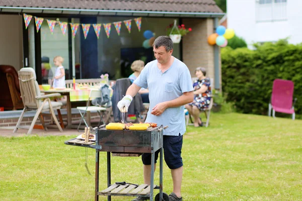 A man cooking meat on barbecue for summer family dinner at the backyard of the house