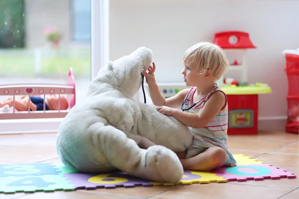 Little girl plays doctor providing healthcare to teddy bear
