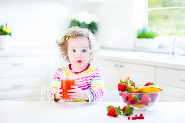 Toddler girl having breakfast drinking juice and eating corn flakes with strawberry