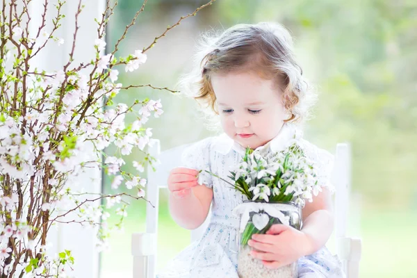 Girlsitting in a white rocking chair holding first spring flowers
