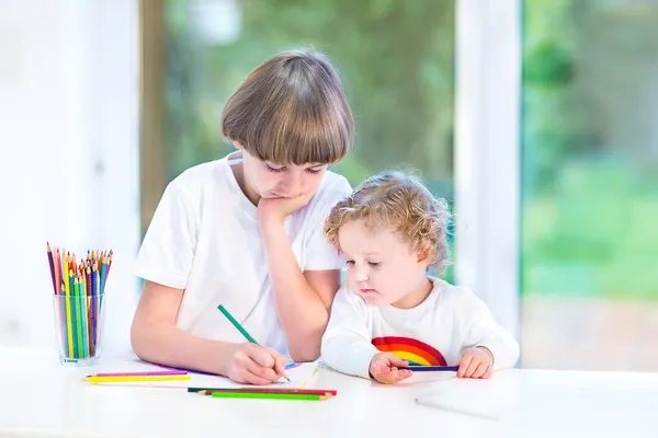 Toddler girl sitting on a white desk watching her brother drawing
