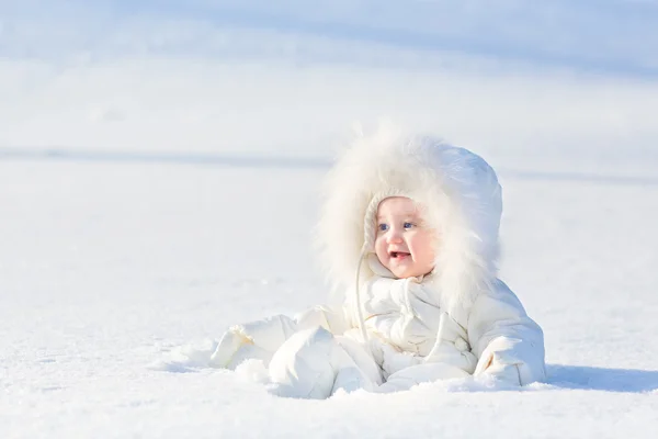 Baby girl in a warm white snow suit playing in snow