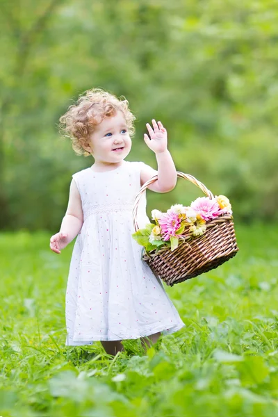 Toddler girl playing in the garden with a flower basket