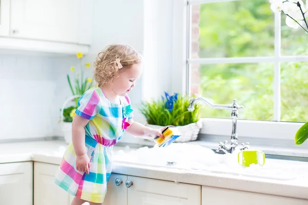 Girl washing dishes, cleaning with a sponge and playing with foam