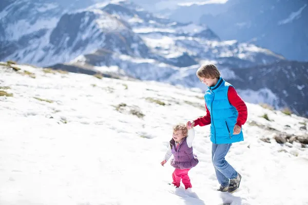 Two children playing together in snow in the mountains