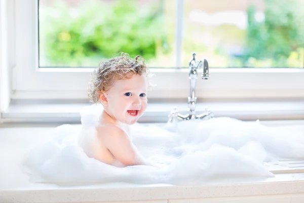 Baby girl with big blue eyes playing in a bath