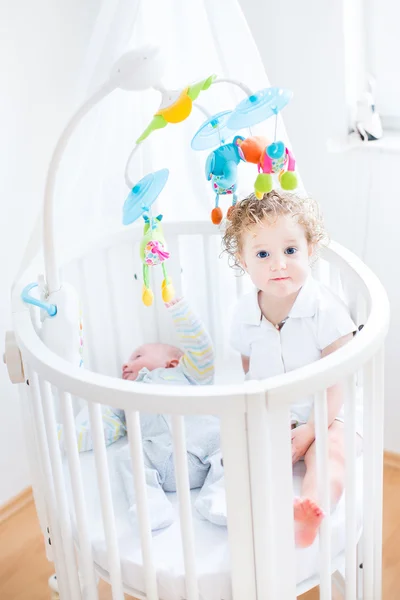 Toddler girl sitting in a crib of her her newborn baby brother