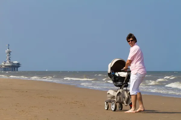Father walking with a baby stroller on a beach