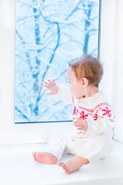 Beautiful baby girl sitting next to a window