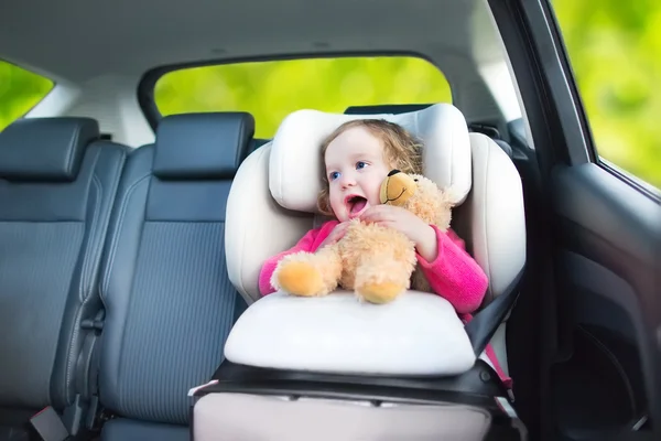 Cute curly toddler girl with a toy bear enjoying a car ride