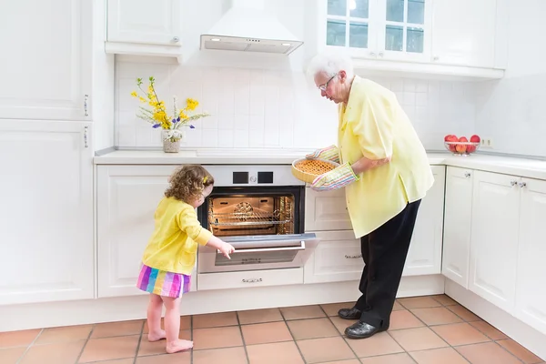 Happy grandmother and little girl baking a pie in a white kitche