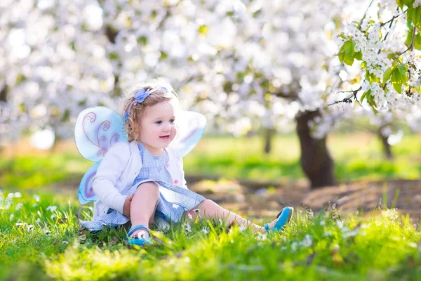 Happy toddler girl in fairy costume in spring apple garden
