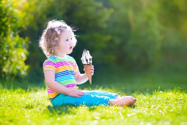 Happy toddler girl eating ice cream in a garden