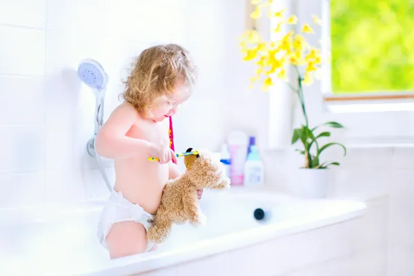 Baby girl brushing teeth playing with a teddy bear