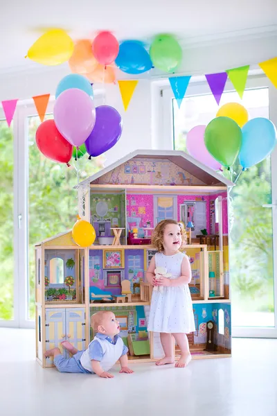 Baby brother and sister playing with a doll house