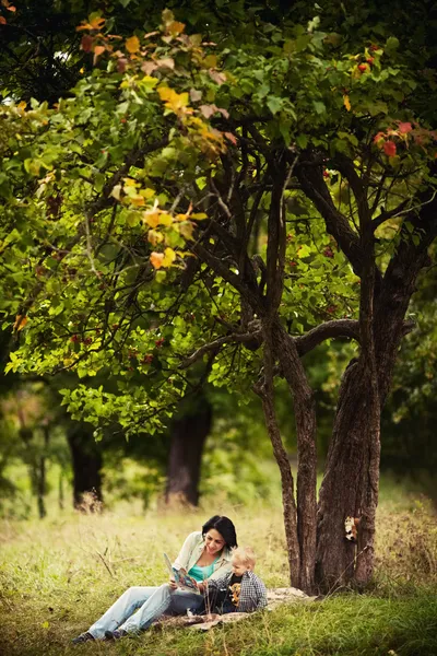 Mom and son with book sitting on green grass in green park. Concept of happy family relations and carefree leisure time