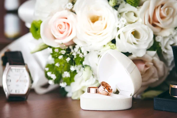 Gold wedding rings in white gift box in shape of heart and wedding bouquet.