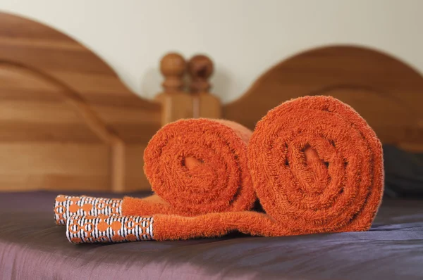 Rolled orange towels on the violet covered bed
