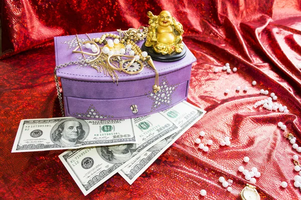 Box for jewelry, dollars and golden Buddha on red background