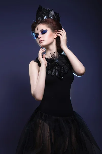Gothic girl with a crown and a necklace of feathers and creative makeup.