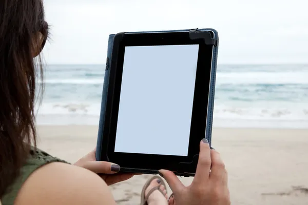 A woman uses a tablet device while on the beach