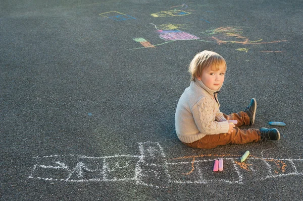 Cute toddler boy drawing with chalk on a nice day