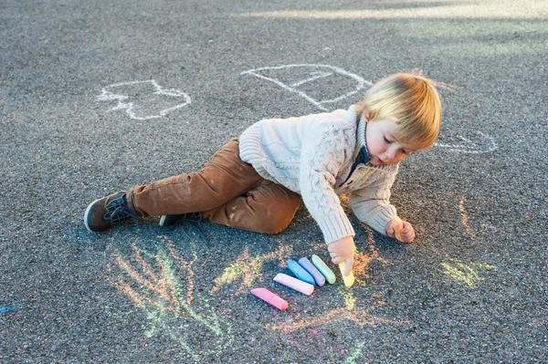 Cute toddler boy drawing with chalk on a nice day
