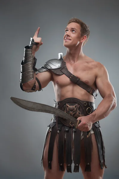 Gladiator in armour posing with sword over grey background