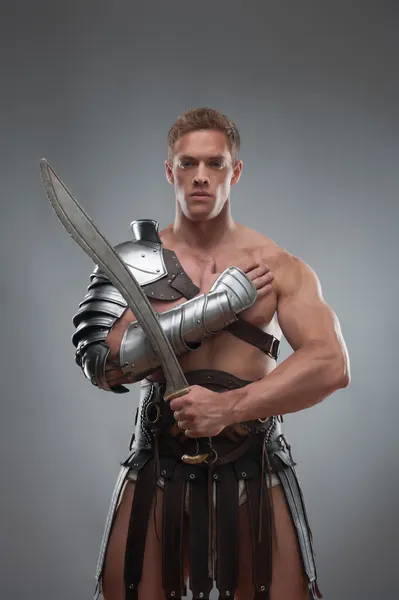 Gladiator in armour posing with sword over grey background