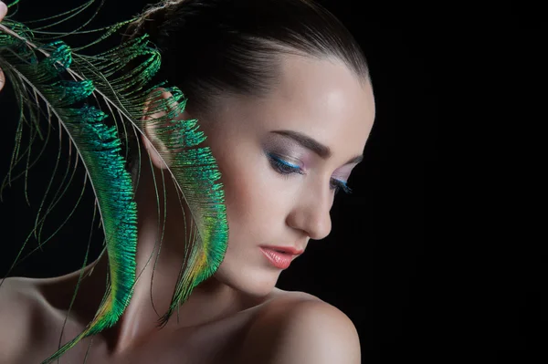 Beautiful brunette young woman with peacock style make-up and pe