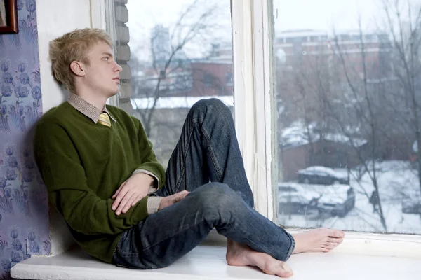 Young handsome man sitting on the window-sill. Student problem. First love