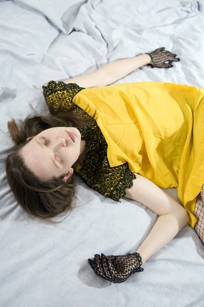 Cute woman in yellow dress lying on bed