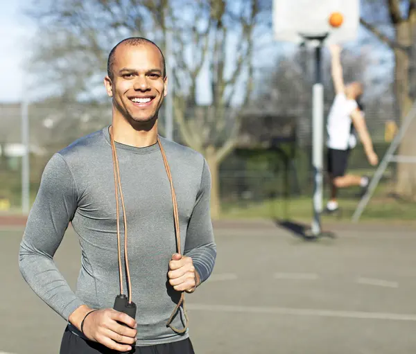 Portrait of a mixed race man smiling to camera whilst holding a skipping rope on an outdoor basketball court