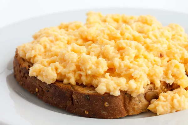 Soft scrambled eggs on brown toast on white plate.