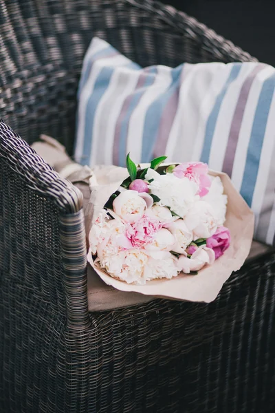 Peonies in a paper bag lying on a wicker chair