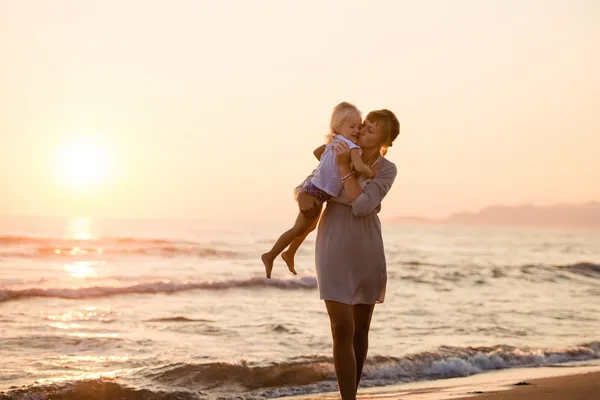 Happy mother kissing her daughter on the beach at sunset, summer