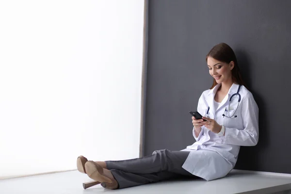 Young woman doctor sitting on the floor with your phone