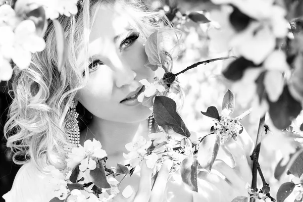 Young beautiful elegant, attractive girl standing in a forest near flowering tree with long hair blond in Sunny day and makeup among flowers