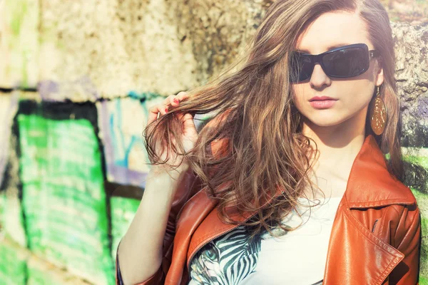 Beautiful brunette girl in sunglasses standing around the walls with graffiti