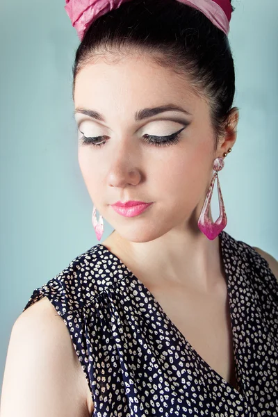 Young beautiful girl in the image retro with a pink bow with beautiful makeup is sitting on a chair in the Studio on a blue background